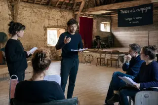 Actors rehearsing in a rustic barn converted into a cultural venue, soft daylight, informal and artisanal atmosphere.