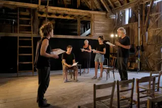 Actors rehearsing in a rustic barn converted into a performance space, wooden beams, simple lighting and props, casual attire, focused atmosphere.