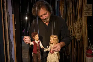 Puppeteer backstage in a community theater adjusting marionettes under soft backstage lighting, surrounded by stage props and curtains, with a focus on the artist's careful hands.
