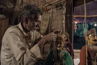 Marionnettist in a dim backstage area preparing handmade puppets, surrounded by rustic props and subdued lighting, evoking the artisanal spirit of rural performing arts.