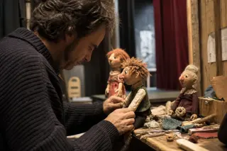 Marionnettist backstage adjusting handmade puppets on a wooden table under soft backstage lighting in a small-town theater