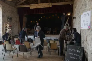Volunteers preparing a simple community performance hall with handwritten signs, stone walls, and soft natural light, conveying a humble backstage atmosphere.