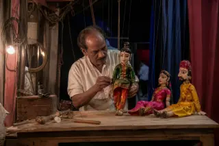 Marionnettiste en coulisse manipulant ses marionnettes, lumière douce et ambiance artisanale dans un théâtre communal