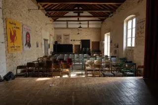 Empty village theatre in Indre-et-Loire seen from stage, morning light, mismatched chairs, hand-painted posters on stone walls, simple artisanal setting.