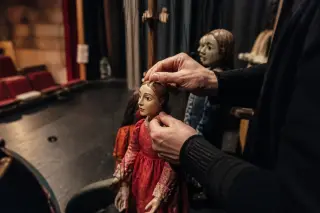 Marionnettist backstage in a small theater adjusting handmade puppets in soft, natural light, close-up on hands, intimate and humble atmosphere.