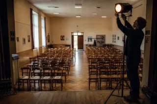 Empty community theater in Touraine viewed from the stage with wooden chairs, soft morning light, and signs of quiet preparation