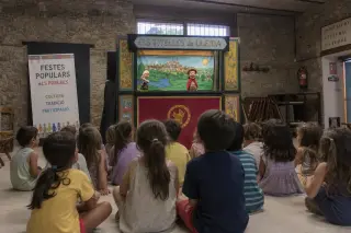 Children seated on the floor attentively watching a colorful puppet theatre in a rural village hall with stone walls and soft natural morning light.