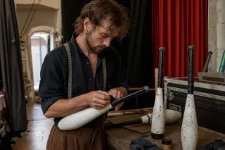 circus artist preparing props backstage in a modest community hall, subdued lighting, showing a raw and authentic rehearsal atmosphere